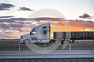 Profile of the gray big rig semi-truck with extended cab transporting boxes on the flat bed semi trailer driving on the flat photo