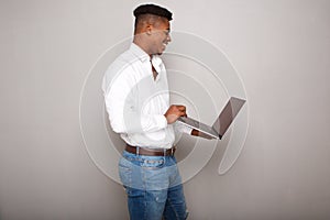 Profile of happy young black man holding laptop computer by gray wall