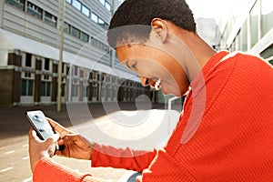 Profile of happy young black woman sitting in city and looking at mobile phone