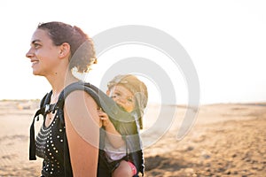 Profile of a mother holding a baby in her back with a baby carrier outdoors