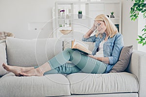 Profile photo of attractive aged mature homey lady sitting comfy sofa couch barefoot reading interesting historic novel