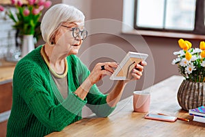 Profile photo of attractive elderly woman touching photo in frame