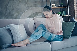 Profile photo of pretty lady suffering from pms holding hands on hurted belly sitting sofa wearing pullover and jeans in
