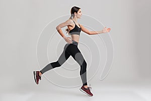 Profile picture of energetic caucasian female in sportswear running, isolated along gray background