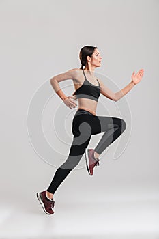 Profile picture of well-built athletic female runner in sportswear training, isolated along gray background