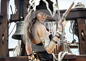 Profile of a Pirate female captain standing on the deck of her ship with pistol in hand.