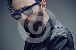 Profile portrait of a bearded brutal man in sunglasses and leather jacket, isolated on a dark grey background.