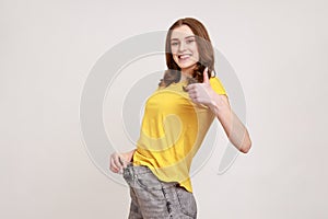 Profile portrait of beautiful happy teenager girl have willpower showing slim waist in big trousers