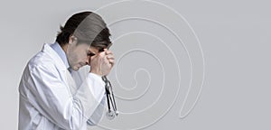 Profile portrait of depressed overworked male doctor with stethoscope in hands