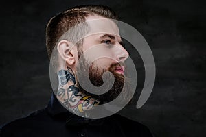 Profile portrait of an expressive bearded man with tattoos on his neck, on a dark background.