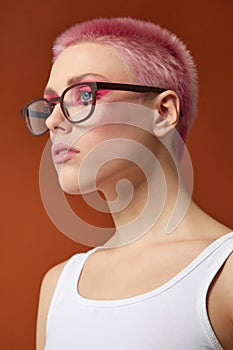 Profile portrait of a girl with pink short hair in red sunglasses, over brown background