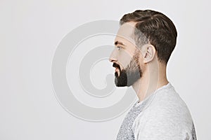 Profile portrait of handsome bearded adult european man with trendy haircut, standing over gray background. Hairdresser