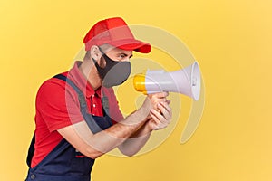 Profile portrait of handyman in unionalls and protective medical mask holding loudspeaker, warning about social distance and