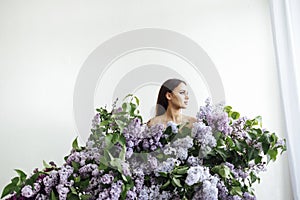 Profile portrait of a happy young woman in a white shirt by bouquets of lilacs all arounded her