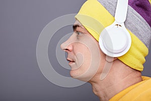 Profile portrait of serious concentrated man wearing yellow hoodie, beanie hat headphones standing isolated over gray background,