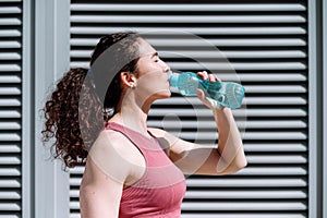 Profile portrait of sporty woman drinking water in plastic bottle