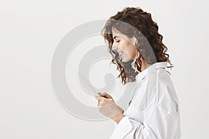 Profile portrait of stunning expressive young caucasian girl wearing wireless earbud and reading news in tablet, smiling