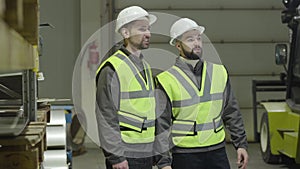 Profile portrait of two Caucasian men standing at warehouse and talking. Employees working at production site. Plant