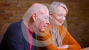 Profile portrait of two senior gray-haired caucasian spouses talk in videochat on laptop being glad and friendly in