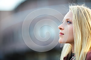 Profile portrait of young beautiful blond woman in city street o