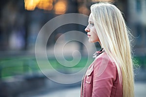 Profile portrait of young beautiful blond woman in city street o