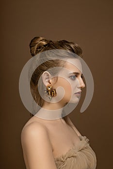 Profile portrait of young and beautiful model wearing golden earrings. Trendy studio shot in golden tones.