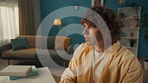 Profile portrait of a young curly guy close up. A man sits at a table against the backdrop of the living room. A man