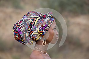 Profile portrait of a young dark-skinned African girl in a national headdress and gold jewelry