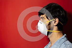 Profile portrait of young guy protect himself from coronavirus with medical flu mask on red background.