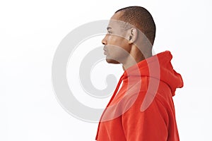 Profile portrait of young handsome african-american man in red hoodie, looking left, standing in queue with no emotions