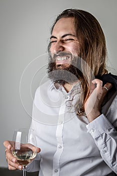 Profile portrait of a young middle eastern businessman with beard and long hair laughing cheerfully while holding a wineglass