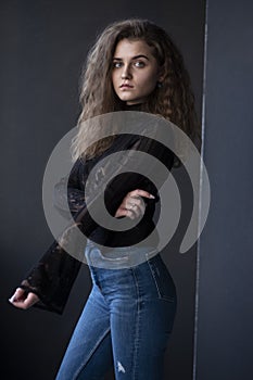 Profile portrait of a young woman, dressed in a black suitcase and jeans, over grey background.