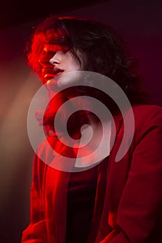 Profile portrait of young woman with makeup and hairstyle, wear red suit, with closed eyes, red neon studio light.