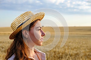 Profile portrait of young woman in straw hat in wheat field at dawn