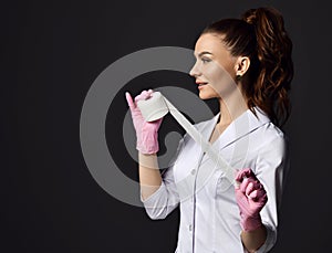 Profile of pretty woman doctor gynecologist or nurse in pink latex gloves and uniform stands holding medical bandage