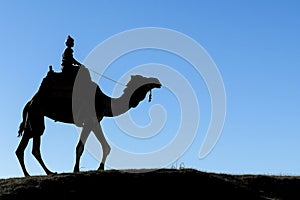profile of rider and camel against a clear, blue sky