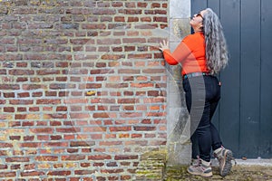 Profile of an senior Latin American woman standing and leaning against brick wall next to closed wooden door