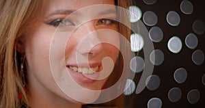 Profile shoot of blonde model with glitter make-up turns to camera and smiles happily on bokeh background.