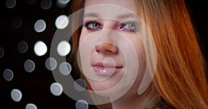 Profile shoot of ginger model with cool make-up turns to camera and watches seductively on bokeh background.