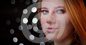 Profile shoot of ginger model with modern make-up turns to camera and smiles positively on bokeh background.