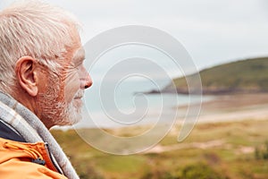 Profile Shot Of Active Senior Man Walking Along Coastal Path In Winter With Beach And Cliffs Behind