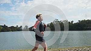 Profile shot following a handsome man running beside lake. Slow motion
