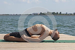 Profile shot of mature man meditating in lotus position on pier against lake