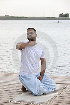 Profile shot of mature man meditating in lotus position on pier against lake