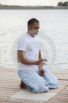 Profile shot of mature man meditating in lotus position on pier against lake