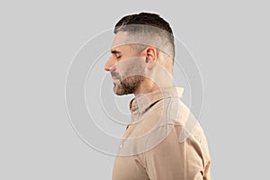 Profile shot of middle aged bearded man in shirt standing with closed eyes over light background, side view, copy space