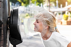 Profile side close-up view cute little blond kid girl enjoy fresh moisturized air blowing from big cooling fan machine