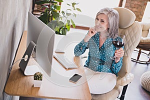 Profile side photo of aged business woman happy positive smile sit desk look computer drink wine rest relax indoors