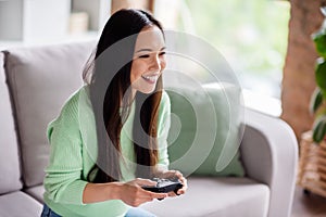 Profile side photo of nice candid korean girl play video game hold joystick enjoy rejoice contest laughing sit divan in