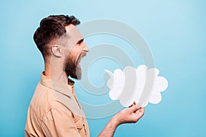 Profile side photo of shouting man holding paper card cloud wearing brown shirt  over blue background